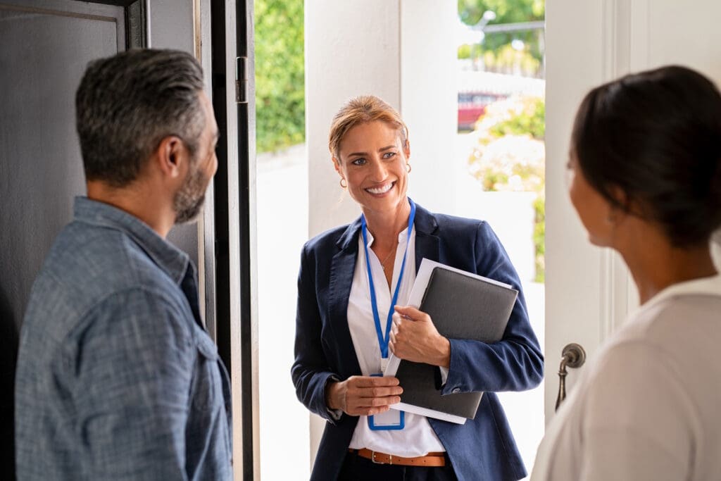 A professional woman engaging with homeowners at their front door, ready for a consultation with her notes in hand.